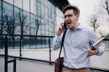 Stressed businessman shouting on phone outside office building