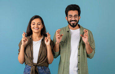 Excited millennial indian couple man and woman wearing casual clothing holding crossed fingers,...