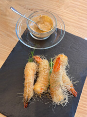 Crispy kataifi shrimp with creamy dipping sauce served on black slate board, top view appetizer...