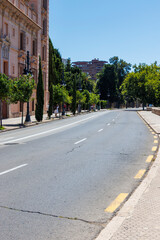 Sunny street view showcasing trees lining a deserted road near a historic building in the background, highlighting city life in the afternoon.