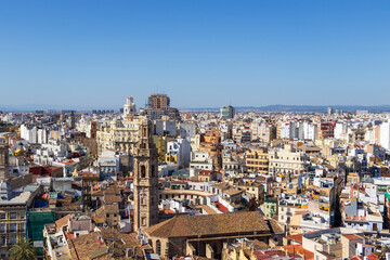 A panoramic view of Valencia showcasing its vibrant cityscape, featuring historic architecture, modern buildings, and blue skies. A busy urban environment filled with energy.