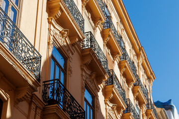 A detailed view of an elegant building's facade in Valencia, showcasing ornate balconies and decorative elements against a bright blue sky. Ideal for architectural projects.