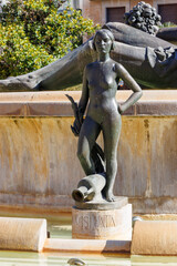 A striking sculpture titled 'Mislata' stands proudly in a fountain surrounded by greenery. The...