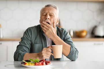 Excessive Daytime Sleepiness. Tired Senior Man Yawning At Table In Kitchen, Elderly Gentleman...