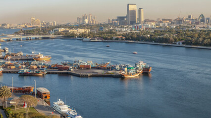 Fototapeta premium Dubai creek landscape timelapse with boats and ship in port and modern buildings in the background during sunset