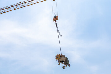 Construction crane lifting concrete mixer against a clear blue sky, showcasing industrial machinery...