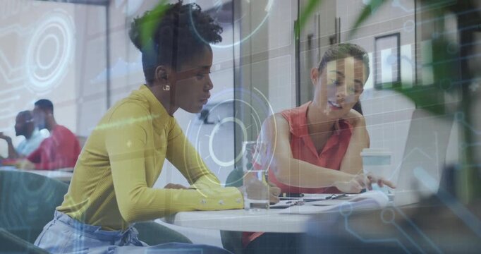 Coworkers opening binder to review charts and marking notes while updating business data on laptop