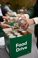 Hands placing can into food drive donation box outdoors , charity donation concept 