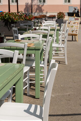 Summer cafe scene featuring green and white tables and chairs arranged neatly under a sunlit outdoor setting, inviting relaxation and social gatherings