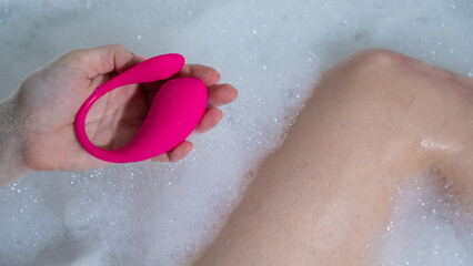 A woman lies in a bubble bath and holds a curved pink vibrator.