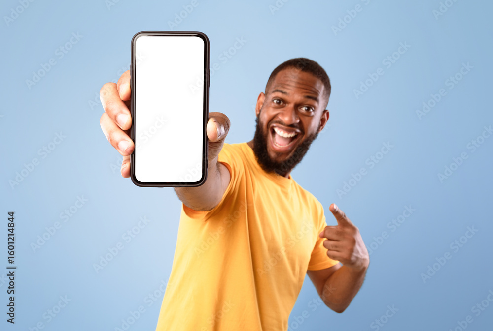 Poster mobile app advertisement. excited black man pointing at smartphone with empty screen on blue studio 