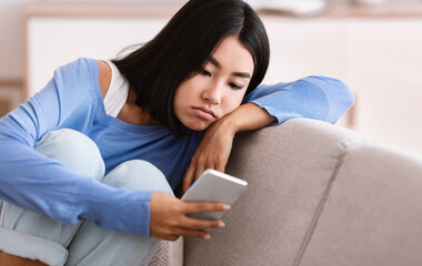 Depression Concept. Portrait of frustrated asian young woman looking at smartphone, checking social...