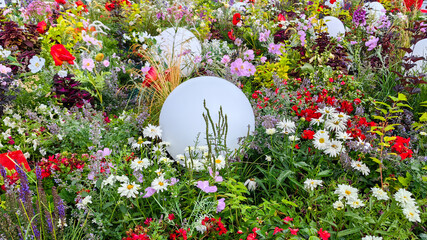 Vibrant flower garden featuring colorful blooms and decorative white spheres nestled among lush greenery, creating a lively and enchanting outdoor atmosphere for nature lovers