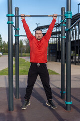 Man in red shirt doing pull-ups at an outdoor gym. The blue sky suggests a sunny day for a workout and active lifestyle