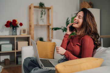 Happy freelancer talking on phone and working on laptop at home