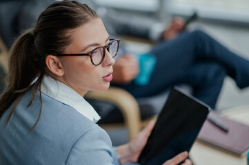 Businesswoman holding tablet and listening during office meeting