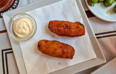 Delicious plate of Spanish croquettes served with creamy dipping sauce on a simple white plate,...
