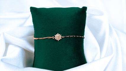 A Rose Gold bacelet with green pillow and a soft white cloth background . A elegant and good looking ladies accessory. From INDIA