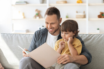 Story time. Loving father reading interesting fairy tales book to his little son, interested...