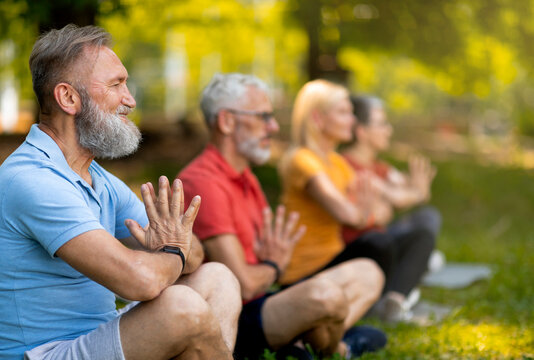 Group of focused seniors practicing yoga in serene park setting, elderly men and women aligned in meditation pose with eyes closed and peaceful expressions, older people meditating outdoors