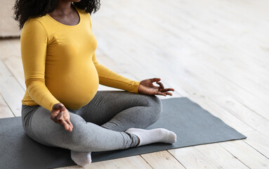 Unrecognizable pregnant black lady meditating at home or yoga studio, copy space. Cropped of...
