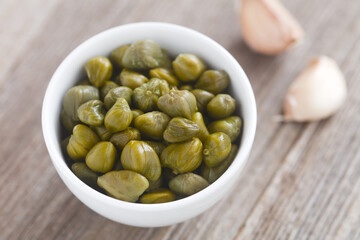 Pickled capers in small bowl with garlic cloves on the side (Selective Focus, Focus one third into...
