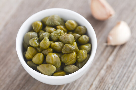 Pickled capers in small bowl with garlic cloves on the side (Selective Focus, Focus one third into the capers)