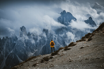 Person in Yellow Jacket Looking Toward Foggy Mountain Peaks from Rocky Terrain in Dre Cime Di Lavaredo National Park, Italy