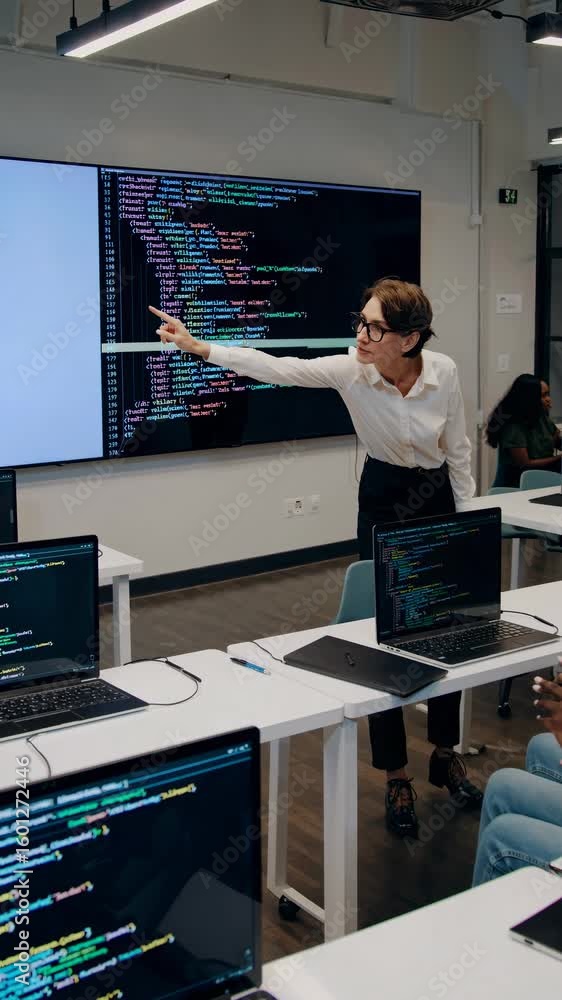 Poster a teacher in a modern classroom explains code on a large screen. the video is shot from a low angle,