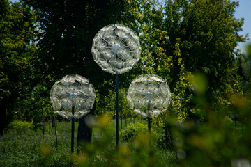 Glass LED spheres perched on metal poles cast dreamy light over greenery in an old city park,...