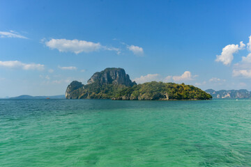 Lush green island with limestone cliffs in turquoise waters, under a clear blue sky, Krabi,...