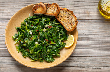 Cooked chicory greens saut&eacute;ed in olive oil with garlic and hot pepper flakes, served with toasted bread and a slice of lemon. A bottle of olive oil on the side. 