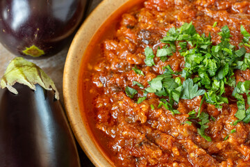Moroccan eggplant and tomato dip (zaalouk) in a bowl, fresh eggplants on the side. 
