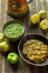 Two typical Mexican salsas: one made of roasted tomatillos and toasted chilies de árbol, and the second made of fresh tomatillos (salsa verde cruda). Raw tomatillos on the rustic wooden table.