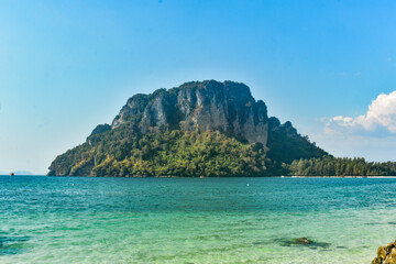 Tropical island with lush greenery surrounded by clear turquoise sea under a bright blue sky, Krabi, Thailand.