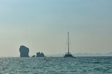 Ocean view with distant islands and a sailboat, bathed in sunlight in Andaman sea.