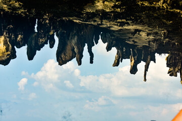 Eerie rock formations hang from a cave ceiling, contrasting with the bright sky and water below.