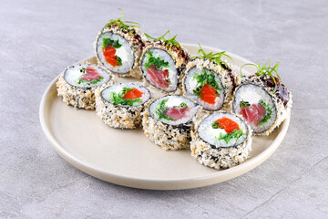 Tempura roll with tuna and spicy sauce on black slate on stone background. Hot sushi roll with chopsticks in contemporary composition. Maki sushi with tuna shavings in minimal style