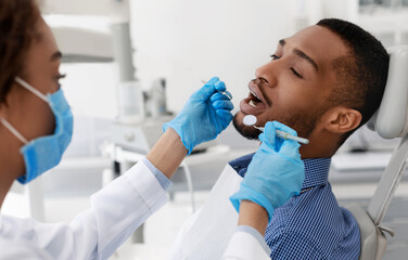 Black guy patient with open mouth having dental treatment from female doctor, close up