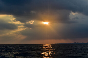 Sunbeams pierce through dramatic clouds, casting a golden reflection on the ocean at sunset.