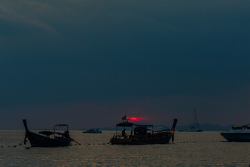 A picturesque sunset over Andaman sea, with Thai traditional longtail boats silhouetted against the...