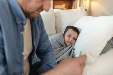 Sick, cold and flu of sick child with caring and loving parent taking temperature of his son. Father on family responsibility leave to care, love and treat his little boy with fever at home.