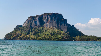 Tropical island with lush greenery surrounded by clear turquoise sea under a bright blue sky, Krabi, Thailand.