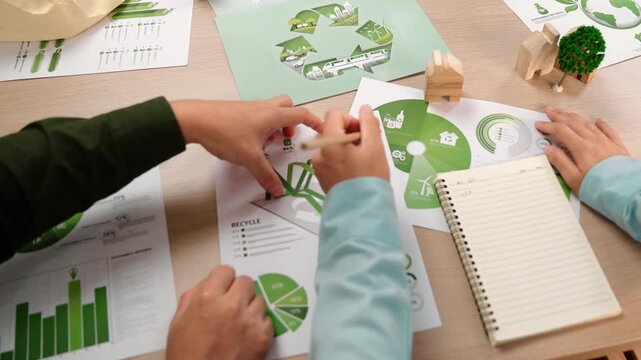 Excellent business people discuss about eco house project on messy table with green energy graph usage choose or analyze alternative power, decrease carbon to save earth. Focus on hand. Delineation.