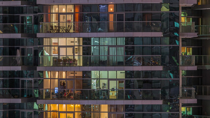 Rows of glowing windows with people in apartment building at night.