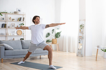 Smiling healthy guy practicing yoga alone at home, morning exercising concept, empty space