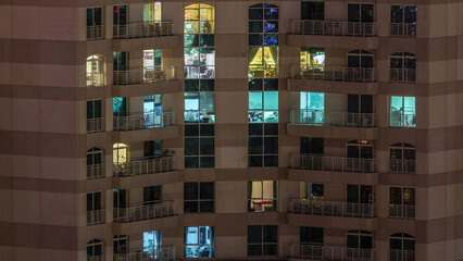 Windows of the multi-storey building with lighting inside and moving people in apartments timelapse.