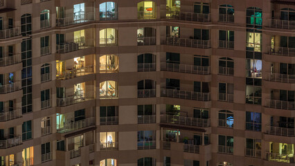 Windows of the multi-storey building with lighting inside and moving people in apartments timelapse.