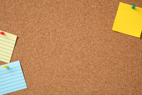 Pinned yellow and blue notes on corkboard with vibrant pushpins. Organized workspace ideal for reminders, planning, and educational content themes