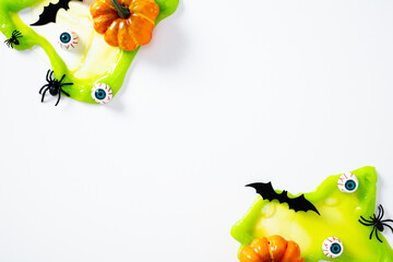Halloween green slime with eyeballs, spiders, bats, and mini pumpkins on white background. Flat lay, top view